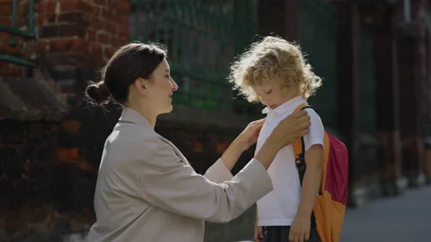 Young mother preparing and caring her little curly son to school outside Stock Footage 202200489