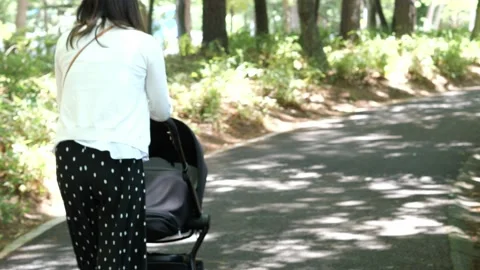 A young mother pushing her baby's pram down a scenic park path. Stock Footage 138074203