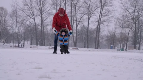 Young mother in red down jacket helps her little baby boy to make his first Stock Footage 106793120