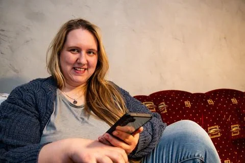 Young mother relaxing on couch while using smartphone in cozy home setting Stock Photos