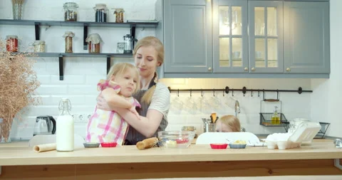 Young mother seating her two daughters at a table for cooking cookies together Stock Footage 132726977