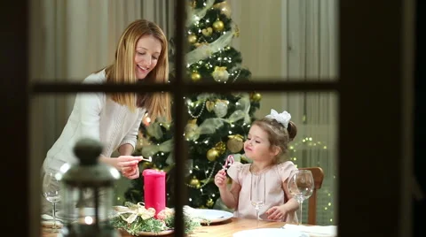 Young mother server festive table, her little daughter eating Christmas candy. Video stock 68539486
