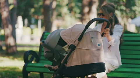 Young mother sitting on a park bench next to a stroller, enjoying a peaceful Video stock 316714022