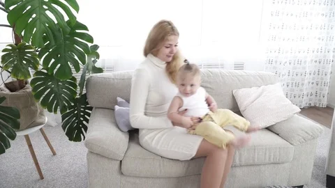 Young mother sitting on the sofa with her small baby boy Stock Footage 73624934
