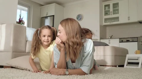 Young mother spending time with two cute daughters, lying on floor at home Stock Footage 152664915