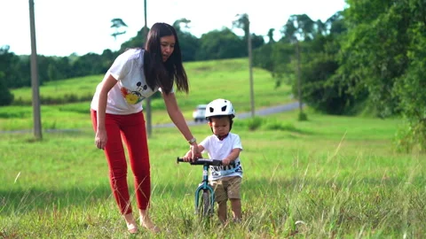Young mother teaching her son to ride the bicycle at natural park. Stock Footage 233282891