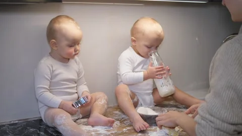 Young mother trying to bake, her twin babies sitting on the table and playing Stock Footage 150298830