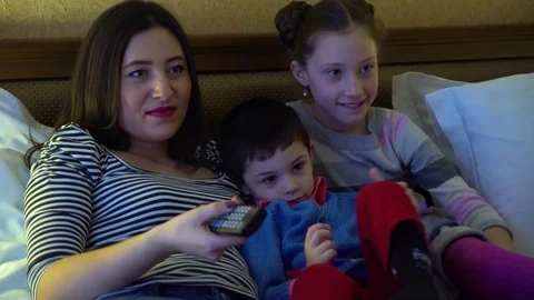 A young mother with two children, lying in hotel in bed and watch TV. Stock Footage 74284412