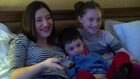 A young mother with two children, lying in hotel in bed and watch TV. Stock Footage 74284467