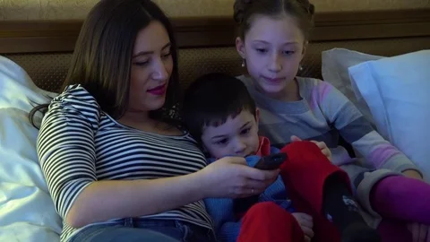 A young mother with two children, lying in hotel in bed and watch TV. Stock Footage 74284558