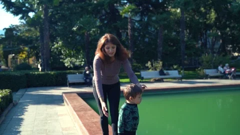 A young mother with a two year old son walks in the city near the pond. Sunny Stock Footage 118548991