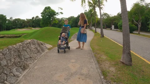 Young mother walking with her two sons in a tropical park, younger baby sitting Stockbeeldmateriaal 344991967