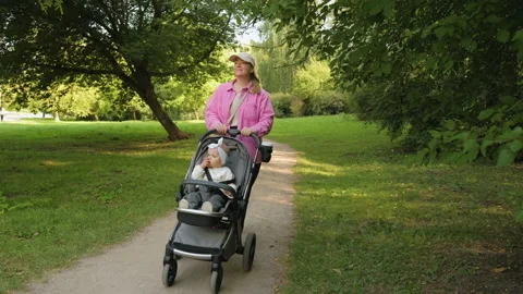 Young mother walking in the summer park with her young daughter in a baby Stock Footage