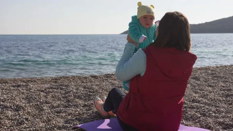 Young mother which sitting on the beach holds her baby in her arms, talks to him Stock Footage 104459712