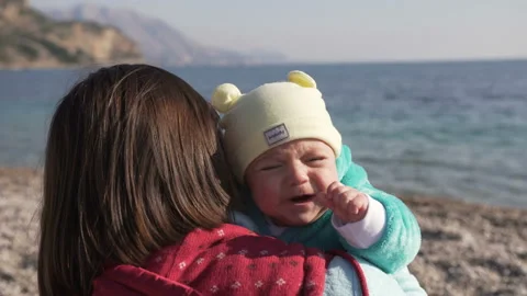 Young mother which sitting on the beach holds her crying baby in her arms Stock Footage 104520959