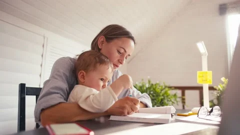 A young mother is working at home using computer while she's taking care of her Stock-Footage 164487114