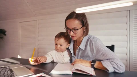 A young mother is working at home using computer while she's taking care of her Vídeos de archivo 164487389