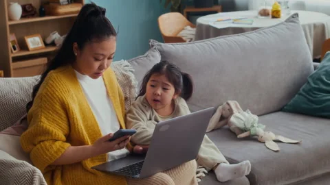 Young Mother Working on Laptop while Babysitting Daughter at Home Stockbeeldmateriaal 307761872