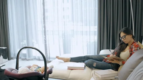 Young mother writes in notebook sitting on couch near baby indoors. Stock Footage 103819140