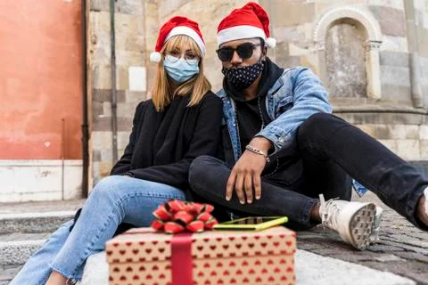 Young multi-ethnic couple exchanges Christmas gifts wearing protective masks Stock Photos