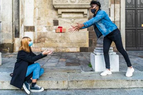 Young multi-ethnic couple exchanges Christmas gifts wearing protective masks Foto stock