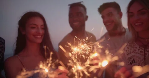 Young multi-ethnic hipsters celebrating with sparklers at summer beach party Stock Footage