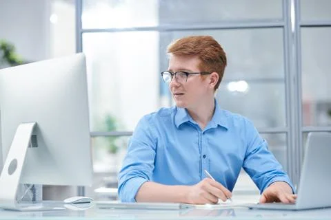Young multi-tasking office manager looking at computer screen Foto stock