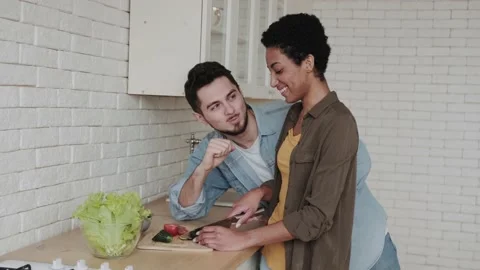 Young multiethnic couple in the kitchen make salad cutting vegetables and feed Stock Footage 236489391