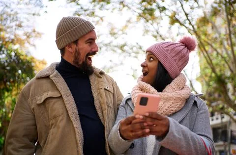 Young multiethnic couple using phone, looking at each other surprised. People Stock Photos