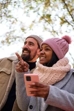 Young multiethnic couple using phone to look for a direction during winter Stock Photos