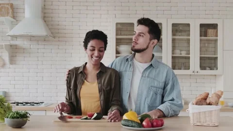 Young multiethnic couple of vegans in the kitchen make salad cutting vegetables Stock Footage 236489247