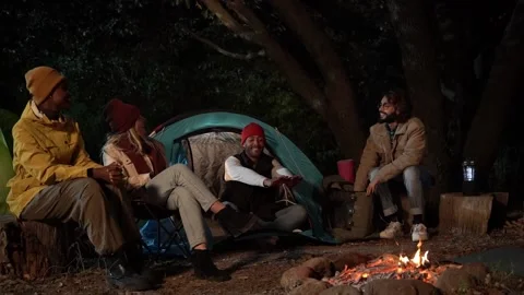 Young multiethnic group of friends camping outdoors sitting around campfire on Stock Footage 232027337
