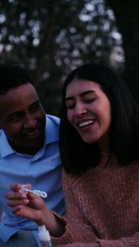 Young multiracial couple blowing soap bubbles together outdoors at dusk Stock Footage 338400399