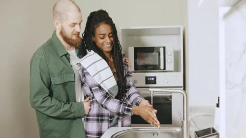 Young multiracial couple enjoying quality time together in kitchen while washing Stock Footage 307406653