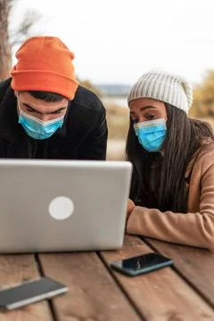 Young multiracial couple of friends using laptop outdoor wearing protective m Stock Photos