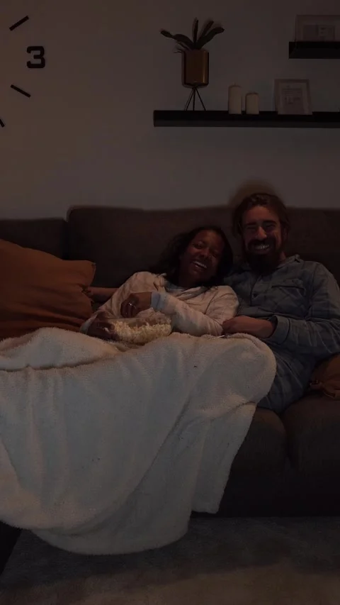 Young multiracial couple having fun watching night movie lying on sofa at home Stock Footage 275176307