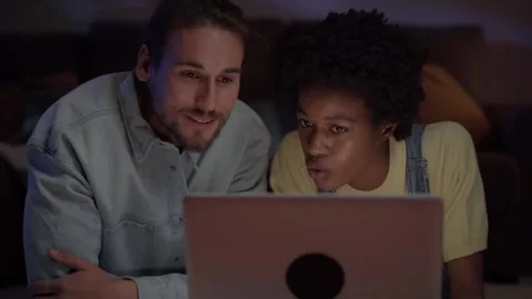 Young multiracial couple looking for ticket sales on computer lying on living Stock Footage 264126670