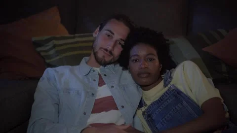 Young multiracial couple in love watching movies TV on living room sofa in Stock Footage 247399490