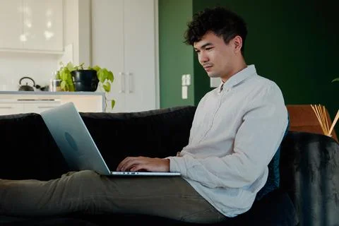 Young multiracial man in shirt using laptop while sitting with feet up on sofa Stock Photos