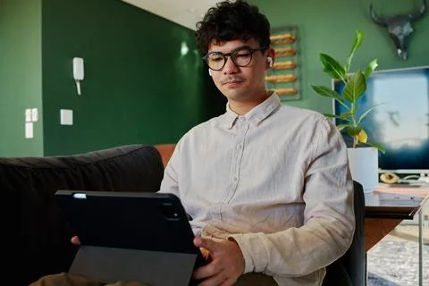 Young multiracial man in shirt using digital tablet with wireless headphones on Stock Photos