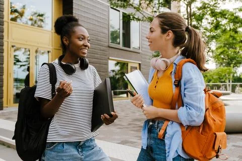 Young multiracial women talking while standing by campus outdoors Stock Photos