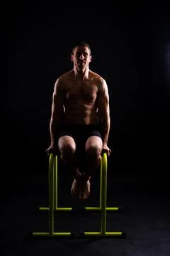 Young muscular man doing parallel bar exercises in dark white red studio with Stock Photos