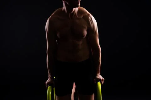 Young muscular man doing parallel bar exercises in dark white red studio with Stock Photos