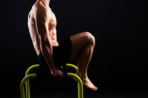 Young muscular man doing parallel bar exercises in dark white red studio with Stock Photos