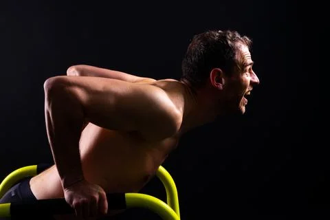 Young muscular man doing parallel bar exercises in dark white red studio with Stock Photos