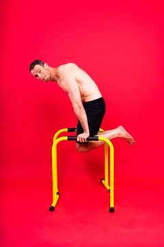 Young muscular man doing parallel bar exercises in dark white red studio with Stock Photos