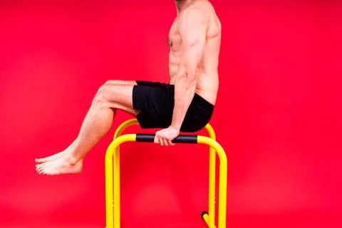 Young muscular man doing parallel bar exercises in dark white red studio with Stock Photos