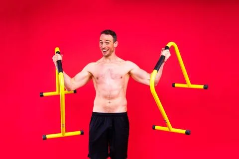 Young muscular man doing parallel bar exercises in dark white red studio with Stock Photos