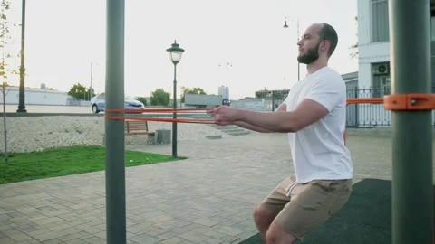 Young muscular man doing pulling exercises with elastic band outdoors. Workout Stock Footage 143503730