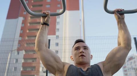 Young muscular man pulls himself up on the horizontal bar of the city playground Stock Photos